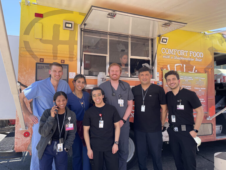 Dr. Kiyan Rad, rounding attending, with his team of physicians and residents in scrubs at a food truck on the grounds of the Tucson VA Medical Center during an on-call day