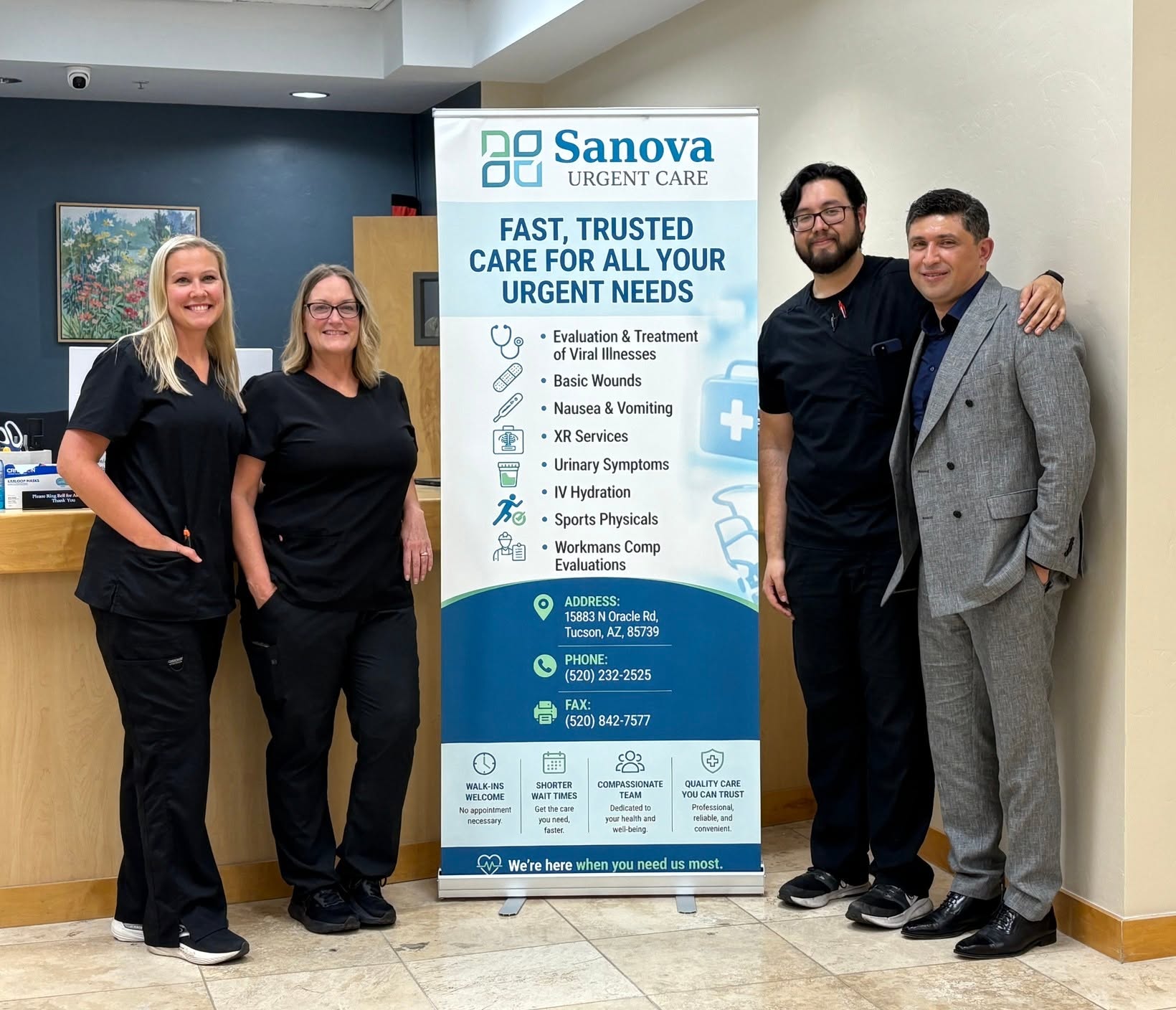 Four staff members stand beside a Sanova Urgent Care banner, smiling for the photo in a clinic lobby.